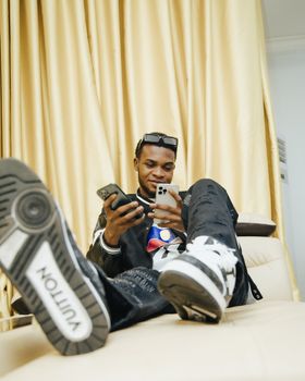 Stylish young man in Lagos leisurely using two mobile phones indoors.