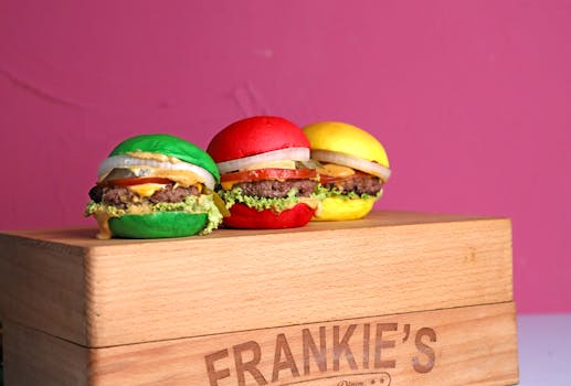 Three vibrant burgers with colored buns on a wooden box against a pink background.