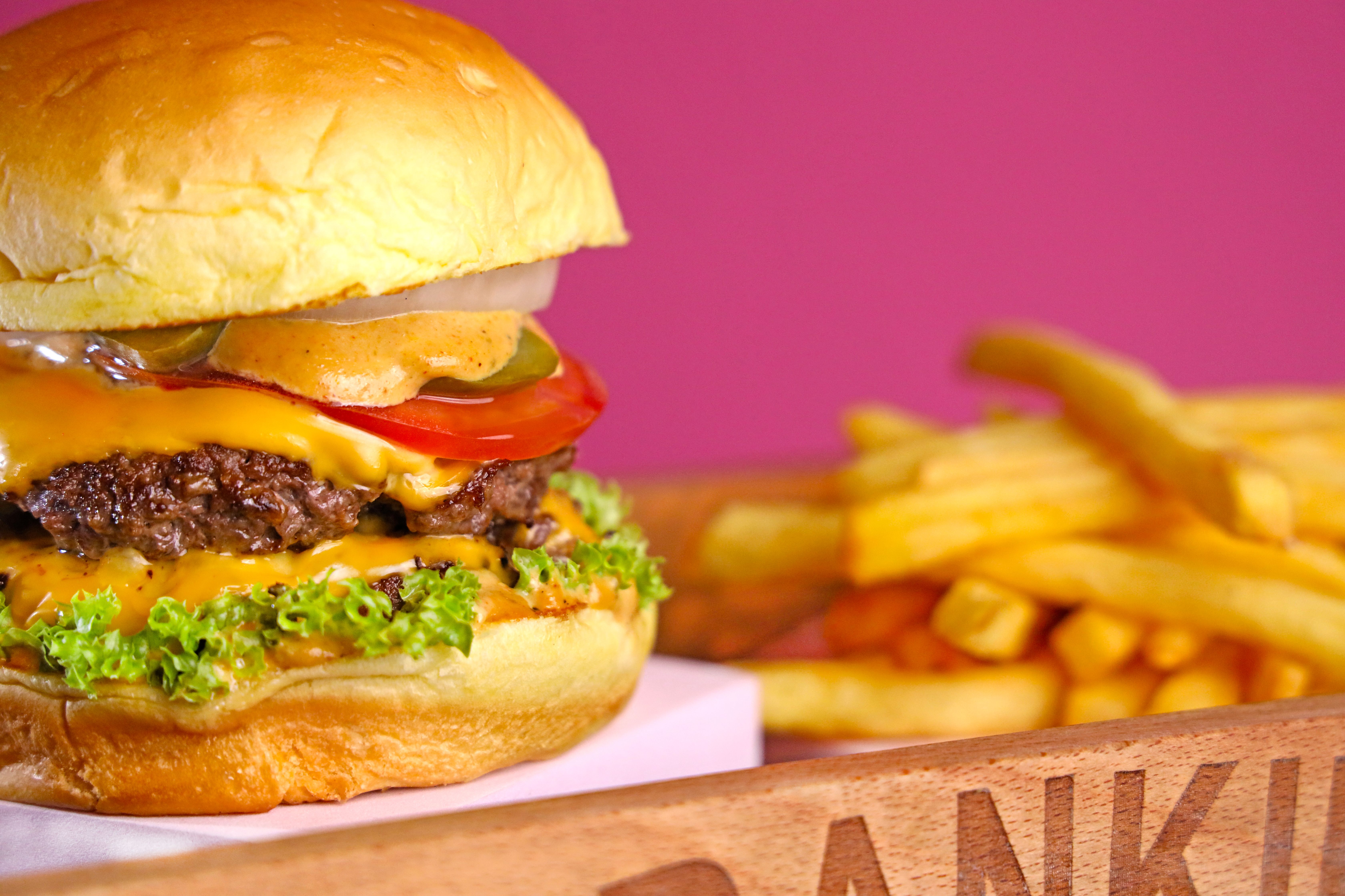 Shameel mukkath - Mouth-watering cheeseburger with fresh ingredients and crispy French fries on a wooden tray.