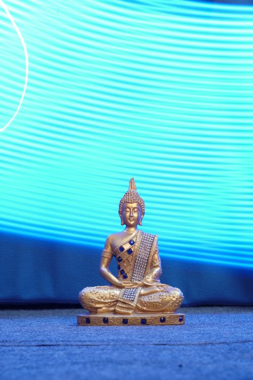 Free A serene golden Buddha figurine against an artistic blue light background. Perfect for meditation themes. Stock Photo