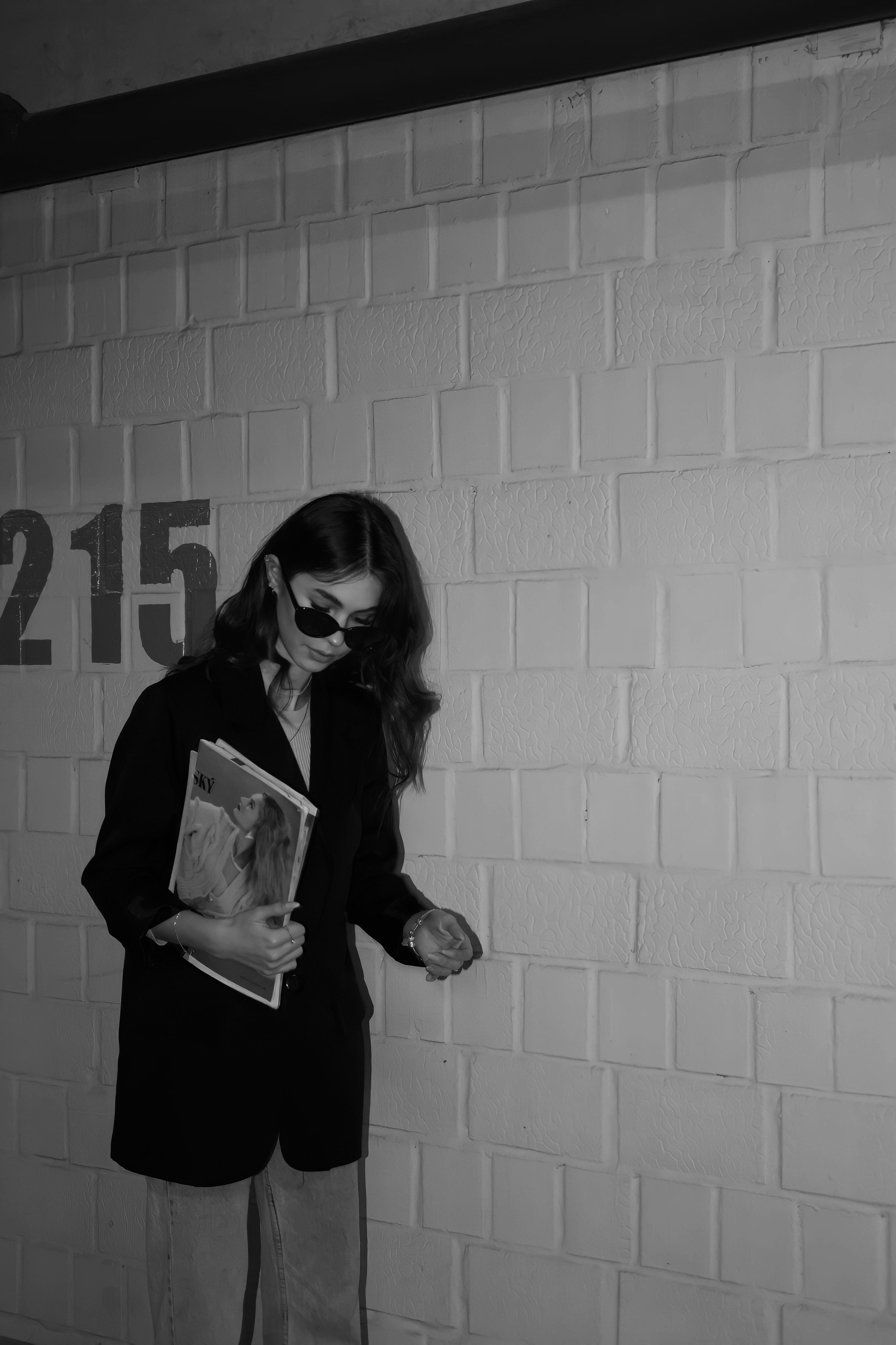 Stylish woman in black and white holding a magazine by a wall.