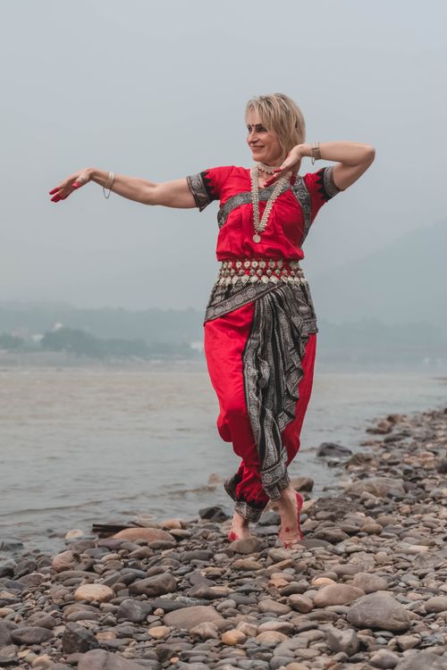 Free Woman performing Odissi dance on a rocky riverbank, showcasing traditional attire. Stock Photo