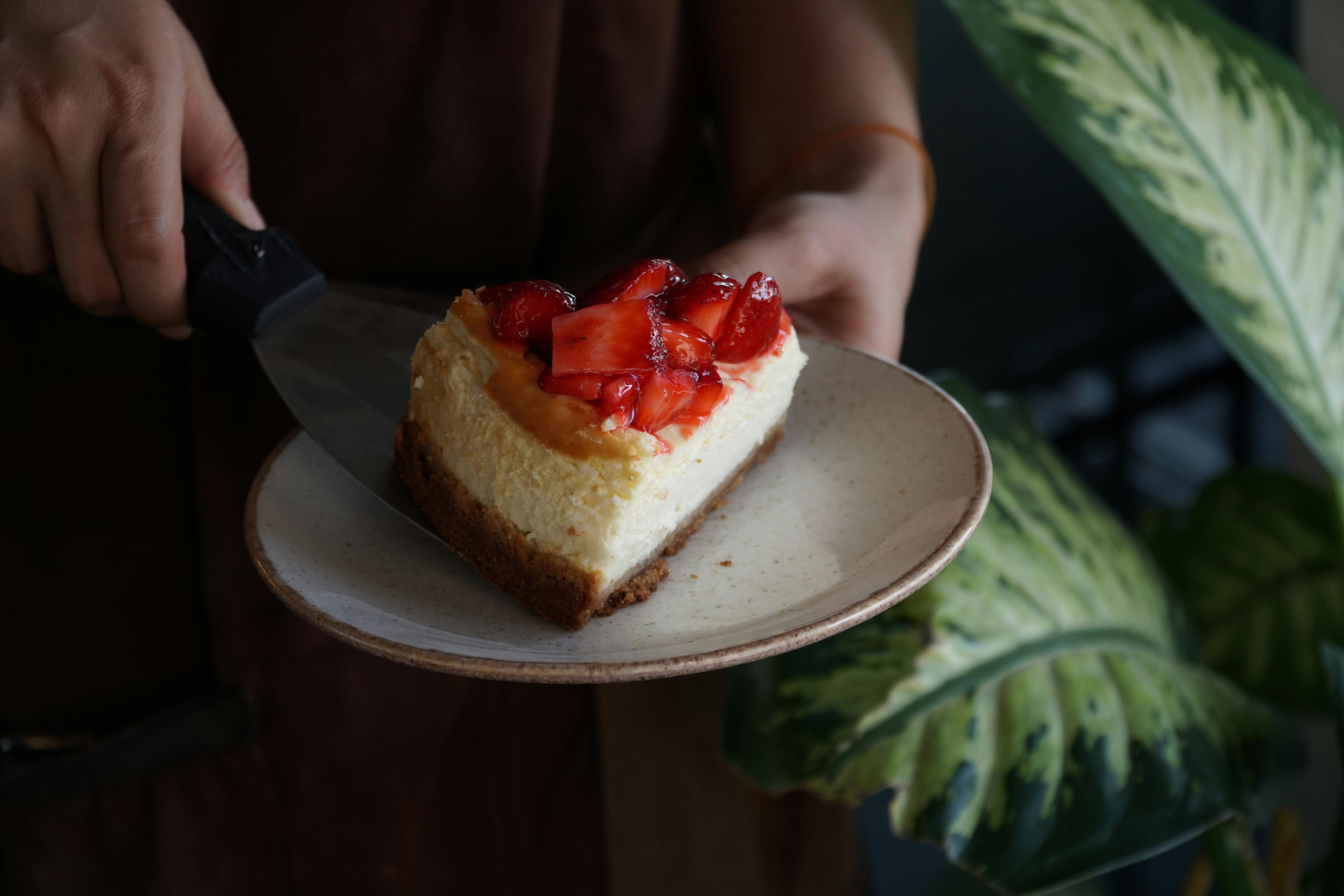 A delicious slice of strawberry-topped cheesecake served on a ceramic plate.
