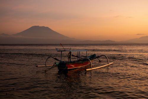 Free A serene view of a traditional boat against a mountain backdrop at sunset. Stock Photo