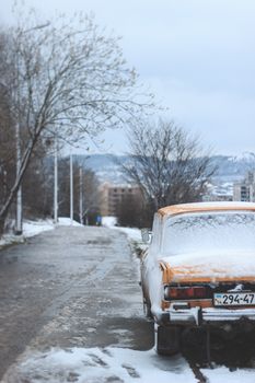 A classic yellow car covered in snow parked on a winter road, evoking a retro feel.