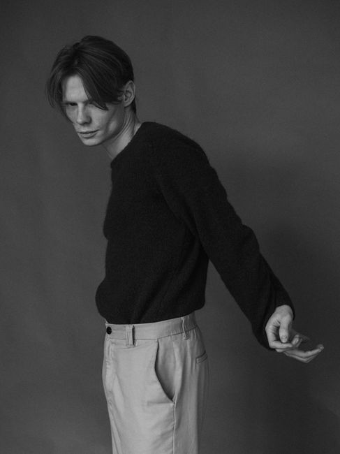 Black and white side profile of a male model posing in a studio setting.