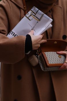 Close-up of a fashionable woman in a brown coat holding a newspaper and handbag in Istanbul.