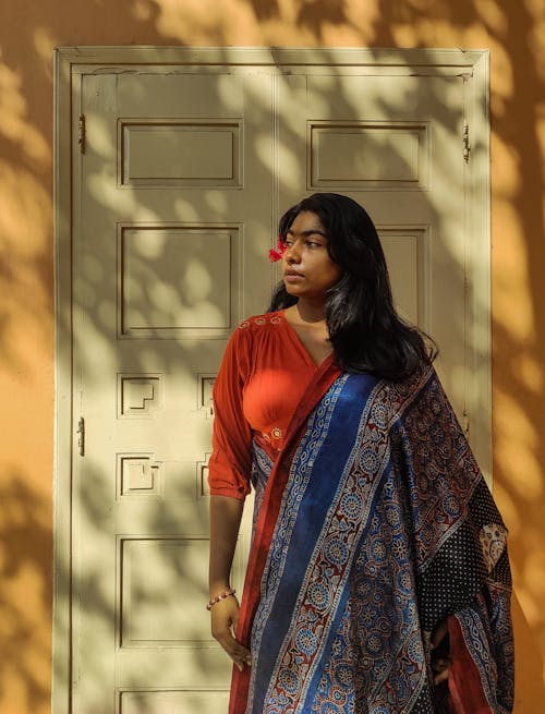 Woman in Orange and Blue Saree Standing beside White Door