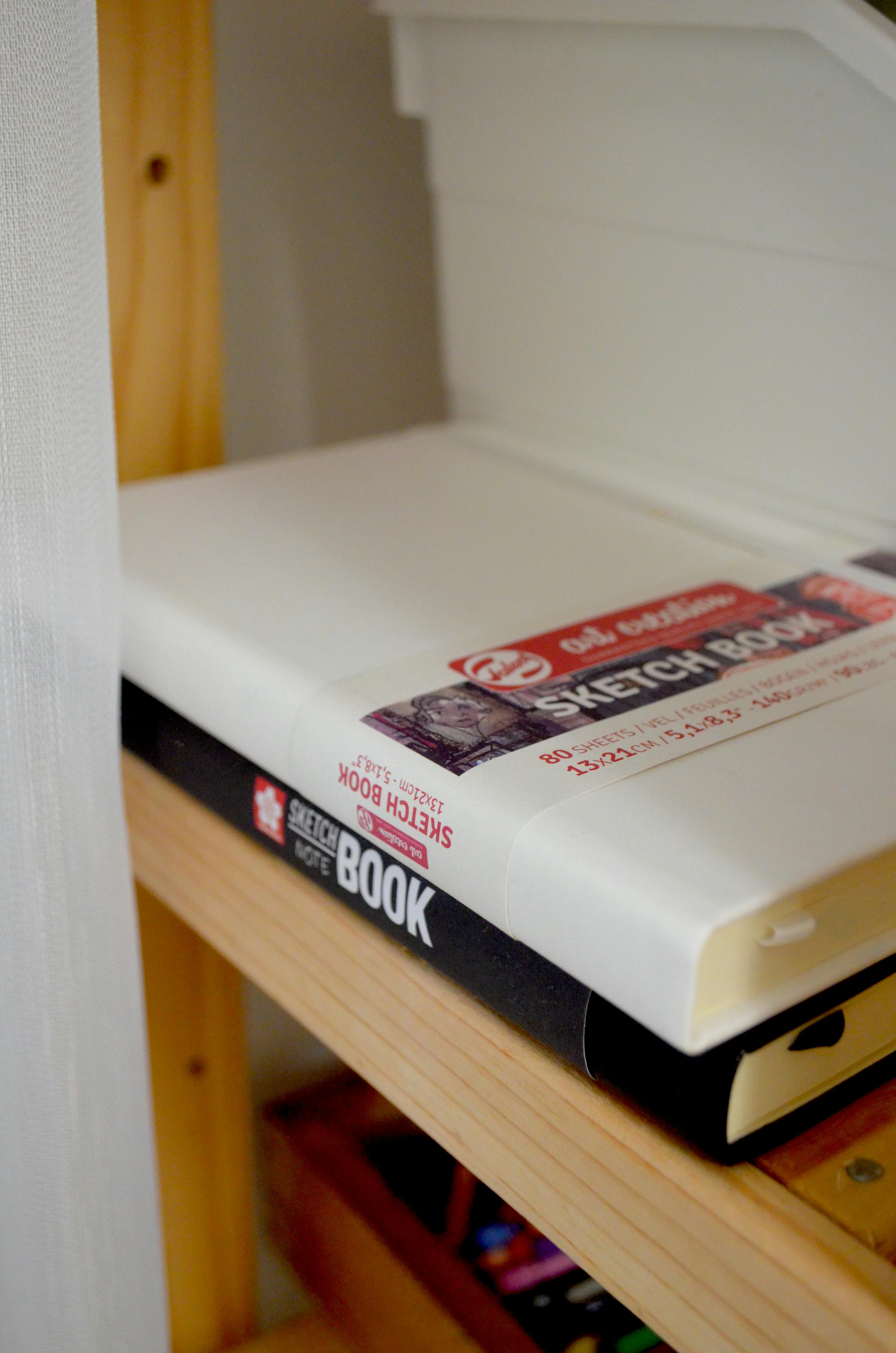 Stack of sketchbooks neatly arranged on a wooden shelf in a creative studio, Istanbul.