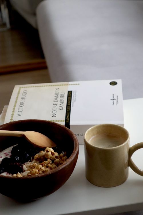 Free A cozy breakfast scene featuring granola, coffee, and a book on a white table indoors. Stock Photo