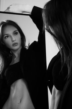 Glamorous portrait of a young woman posing in front of a mirror with a confident pose.