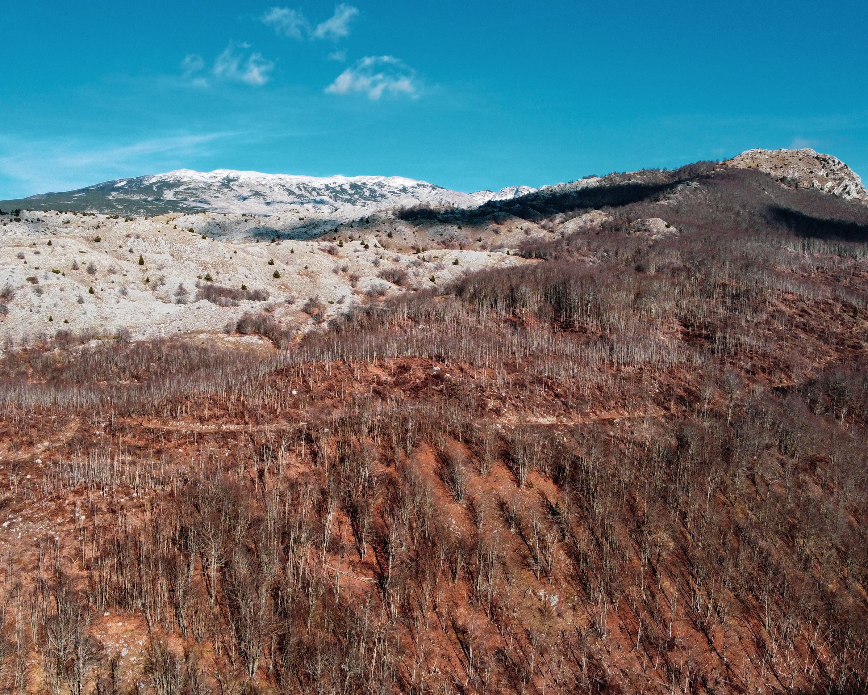 Vibrant aerial shot capturing Bosnian hills and snow-capped mountains under a clear blue sky.