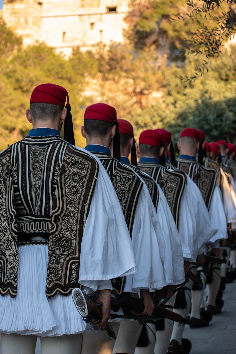 Men In Traditional Costumes Walking In Line Outdoors