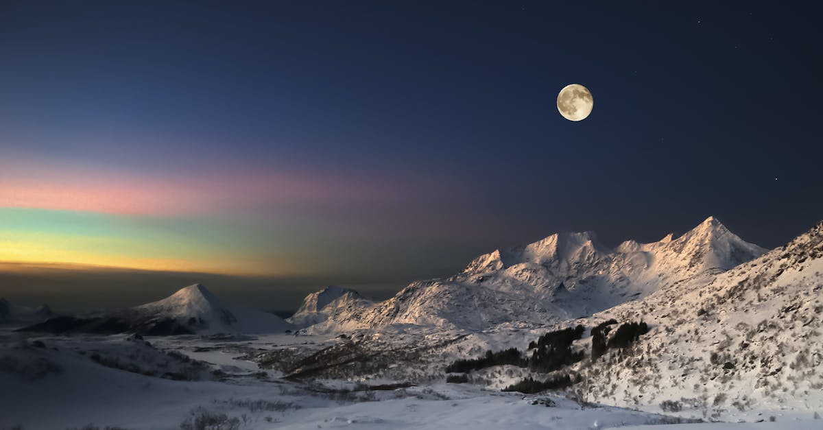 Breathtaking view of aurora borealis over the snow-capped mountains under a full moon.