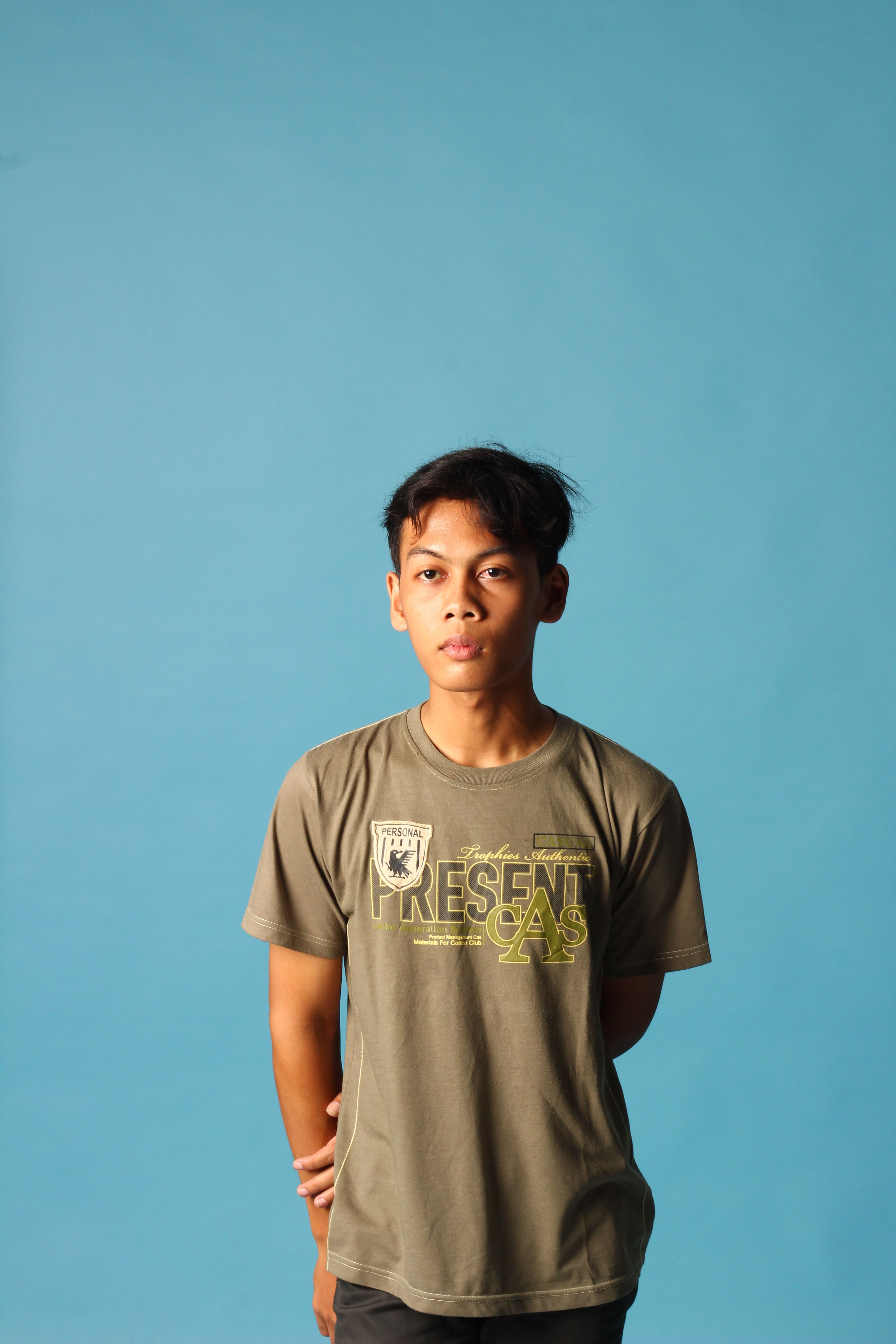 Studio portrait of a young man wearing a green shirt against a blue backdrop.