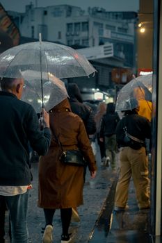 People walking with transparent umbrellas on a rainy street, evening ambiance.