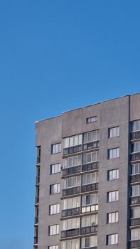 A concrete high-rise building with a modern facade and windows against a clear blue sky.
