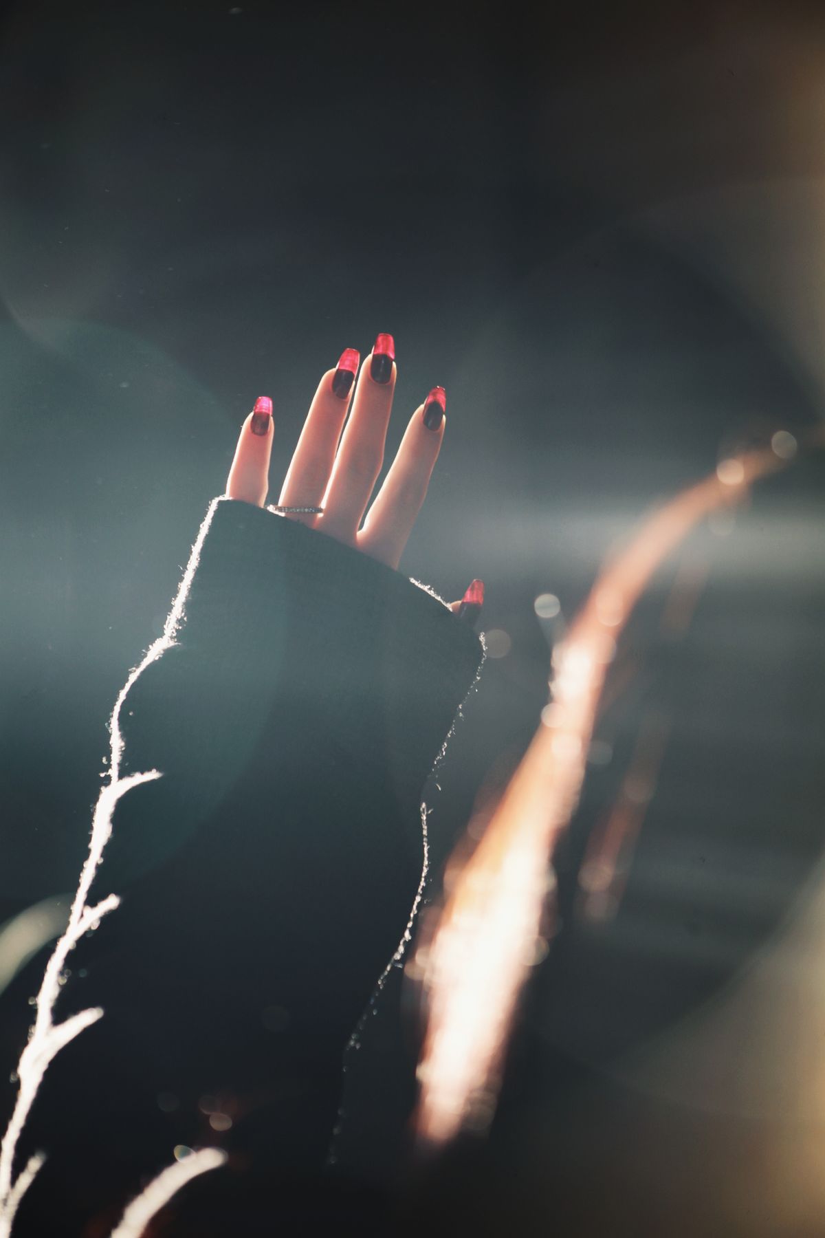 A close-up of a woman's hand with vibrant red nails illuminated by sunbeams, creating a dramatic contrast.