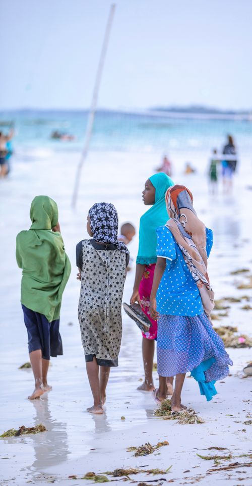 Free A group of girls in vibrant hijabs walking along the sandy beach shore. Stock Photo