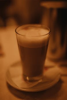 A cozy close-up of cappuccino in a glass with foam and a blurred background.