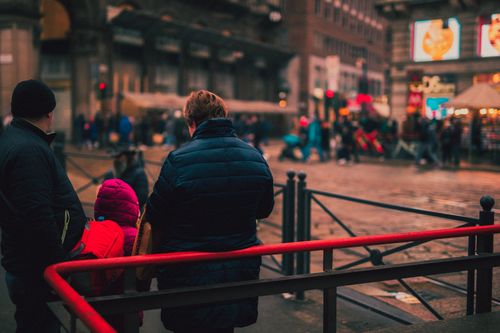 Free A family in warm clothing watches a crowded city scene during winter, captured from behind. Stock Photo