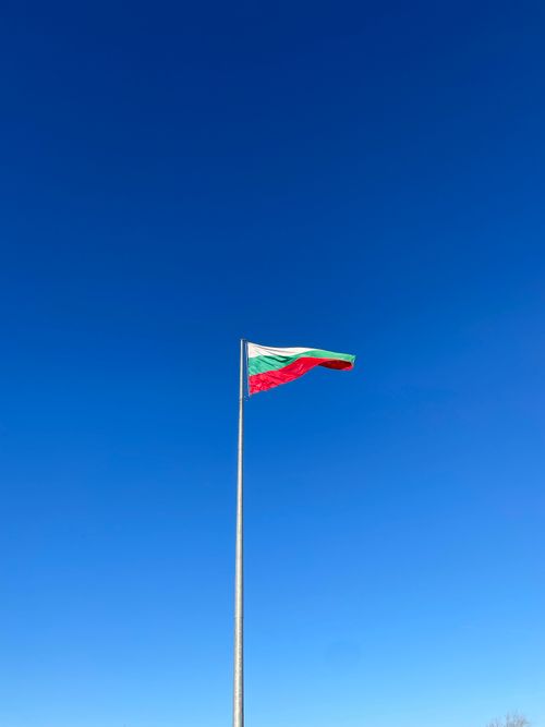 Free The Bulgarian national flag waves proudly on a flagpole against a vibrant blue sky in Vidin, Bulgaria. Stock Photo