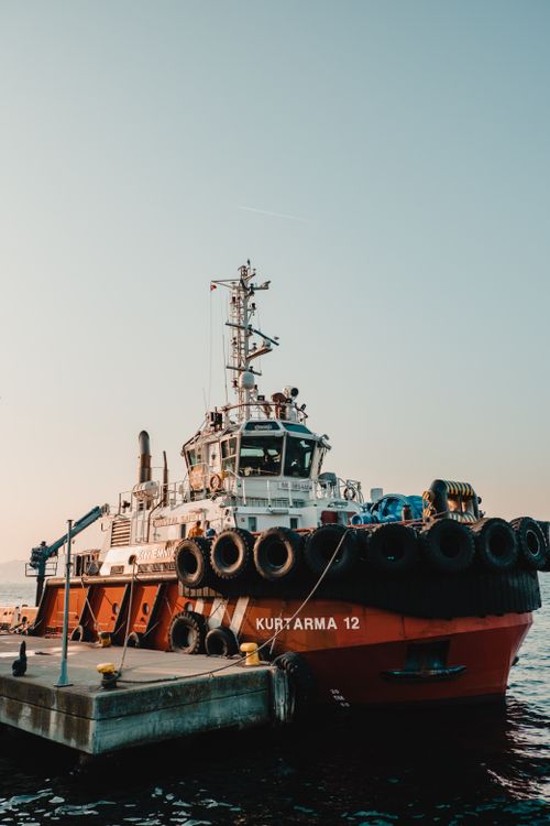 Free A tugboat moored at a dock during sunset with a calm sea backdrop. Stock Photo