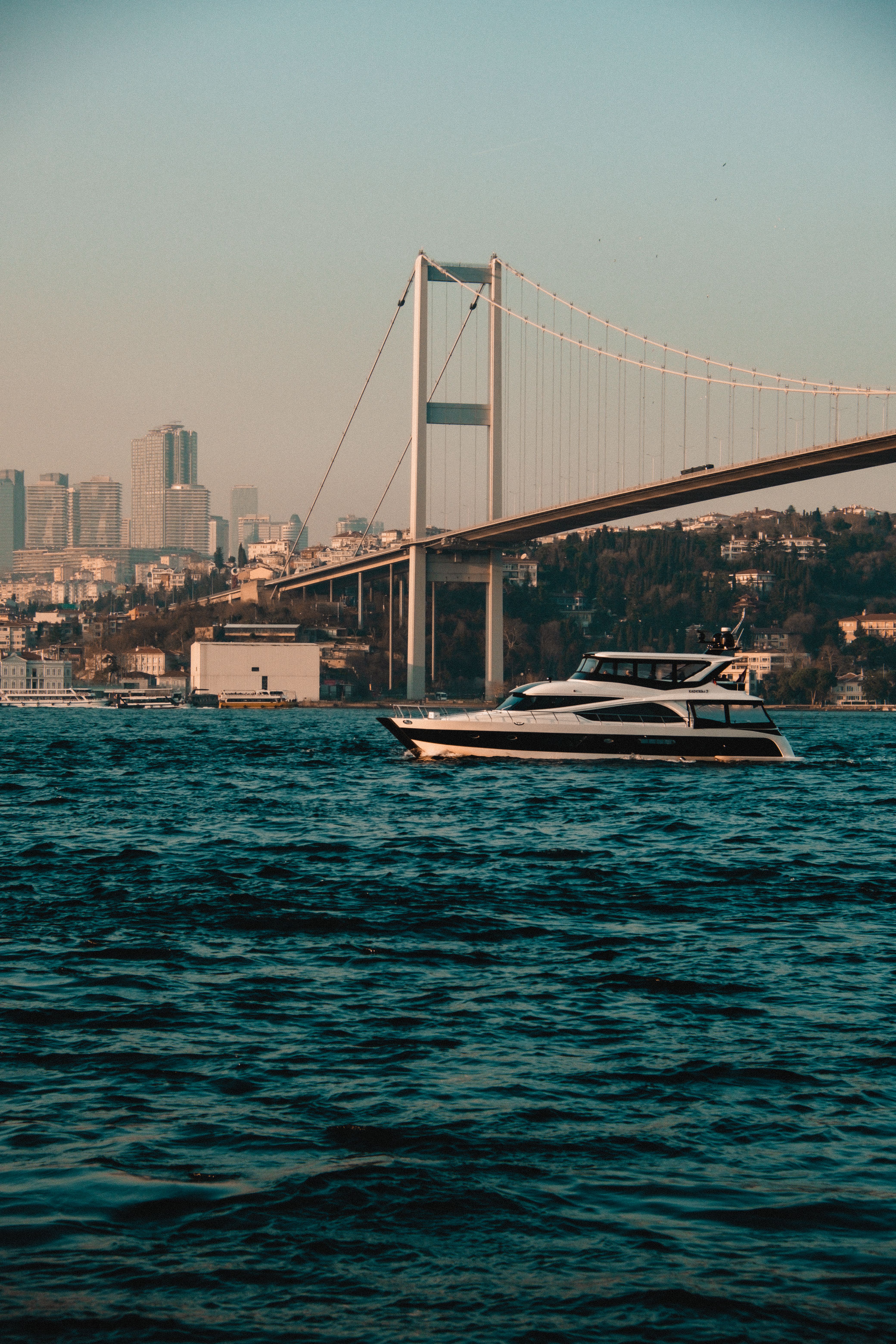 Free A picturesque view of a motor yacht sailing under the Bosporus Bridge in Istanbul at sunset. Stock Photo