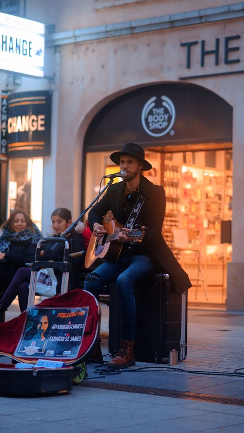 Free A street musician playing an acoustic guitar in an urban setting with a crowd. Stock Photo