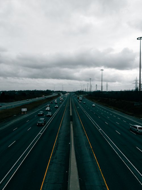 Free Aerial view of highway traffic under cloudy skies, creating a contrasting moody atmosphere. Stock Photo