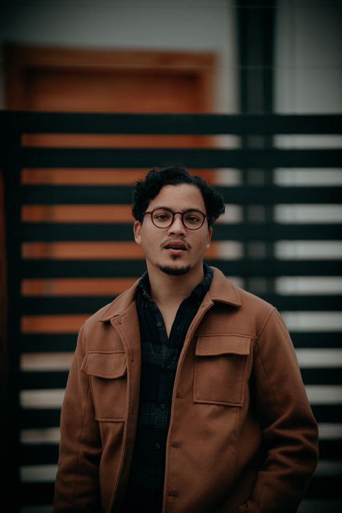 Free A fashionable man with eyeglasses poses confidently in a brown jacket outdoors. Stock Photo
