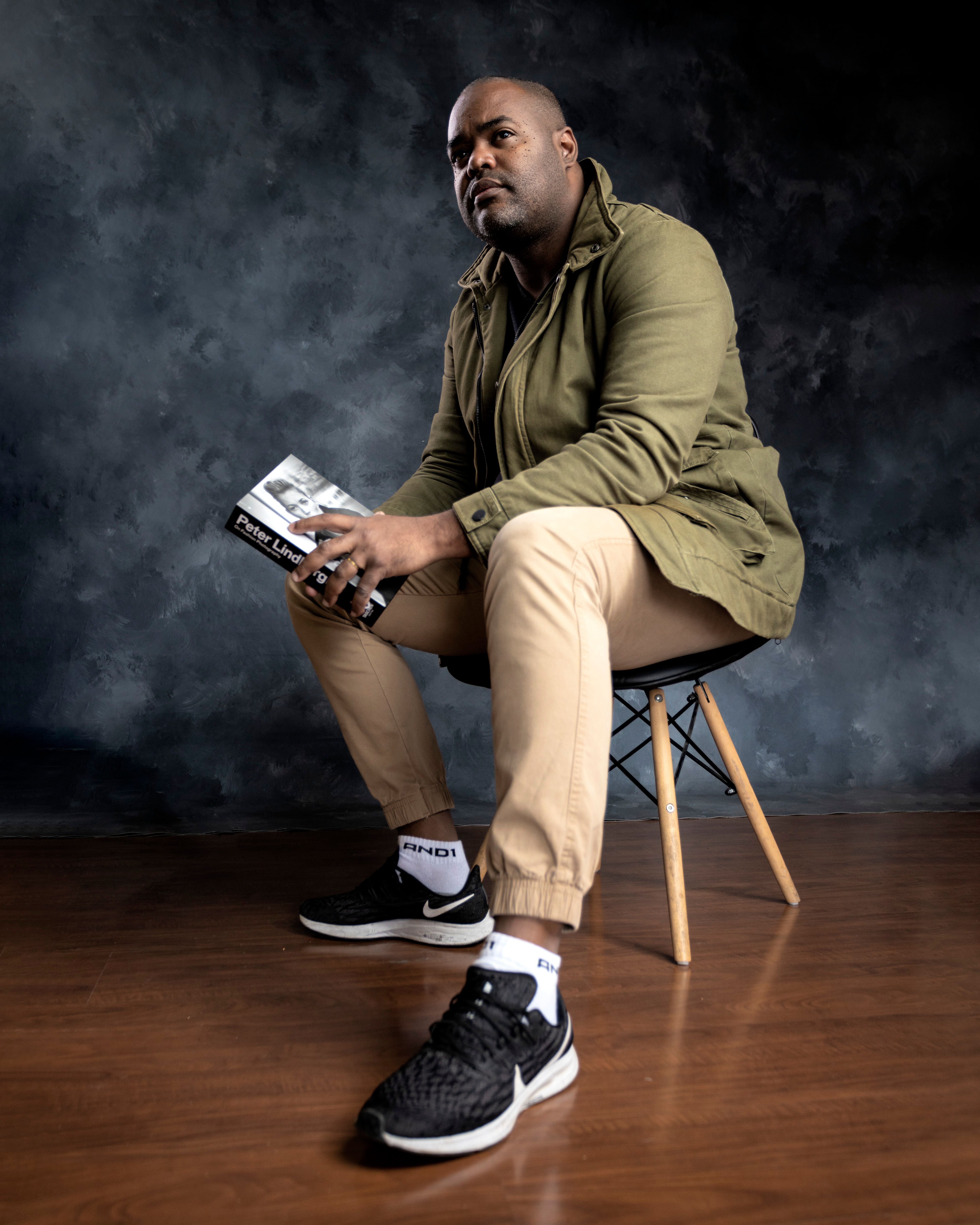 African American man sits thoughtfully with a book in a studio setting.