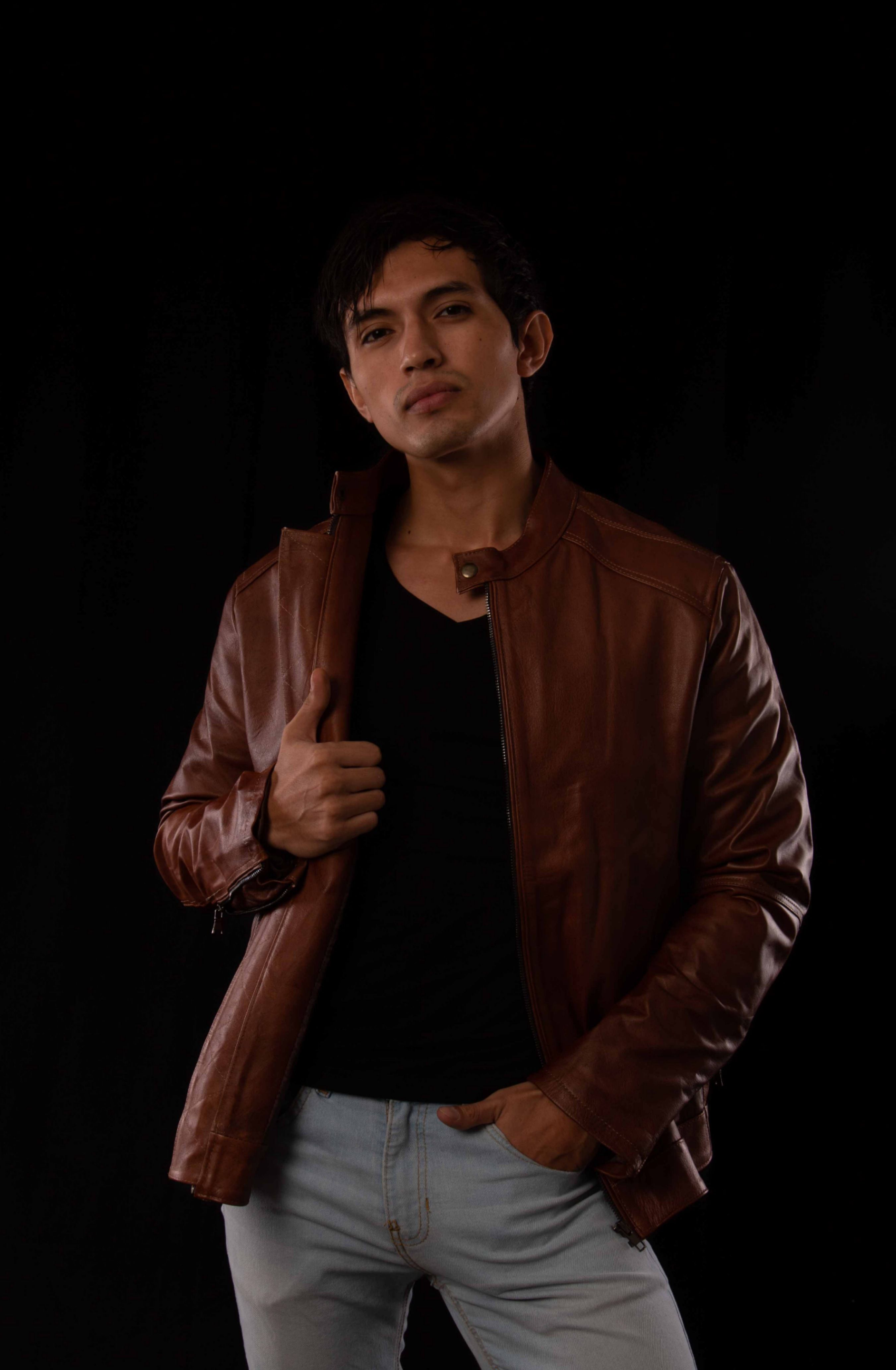 Confident man posing in a brown leather jacket against black background.