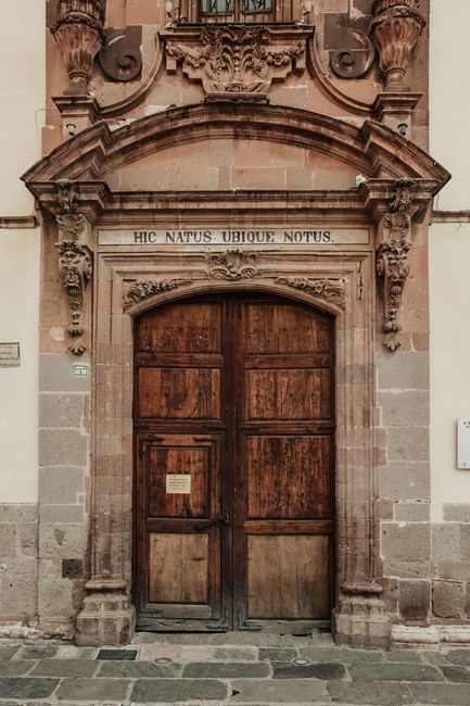A vintage wooden door with ornate carvings and a Latin inscription in an old architectural setting.