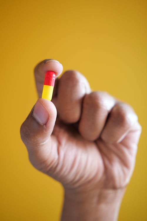 Close-Up Shot of a Person Holding a Capsule on Yellow Background