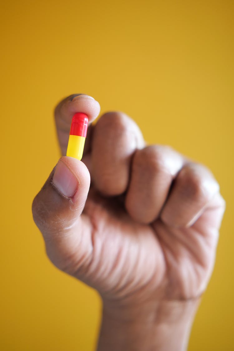 Close-Up Shot Of A Person Holding A Capsule On Yellow Background