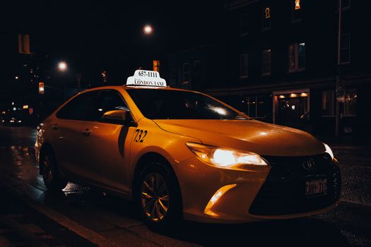 A yellow taxi waiting at night in London, Ontario, Canada. Urban transportation captured with street lights.