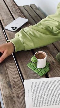 Person enjoying coffee and book on a wooden table outdoors.