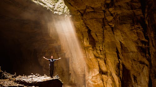 Free Man Standing on a Rock in a Cave with Outstretched Arms Stock Photo