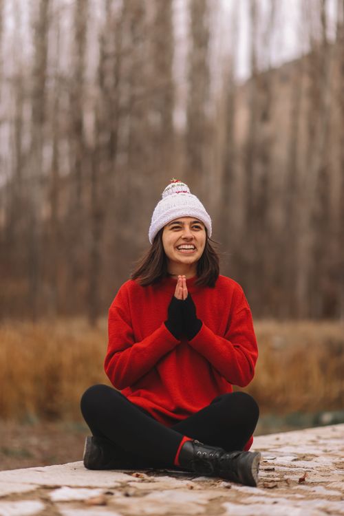 Free A cheerful woman in winter attire, sitting outdoors in nature with a joyful expression. Stock Photo