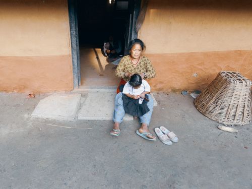 Free A mother braids her daughter's hair outside their rural home, capturing candid family life. Stock Photo
