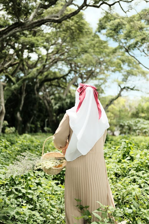 Back View Shot of a Woman Wearing Hijab while Carrying Basket with White Flowers