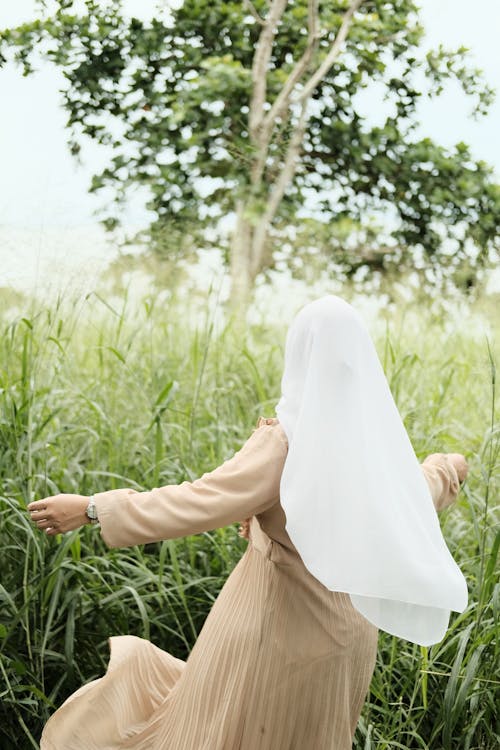 A Woman in White Hijab Walking on a Field with Tall Grasses