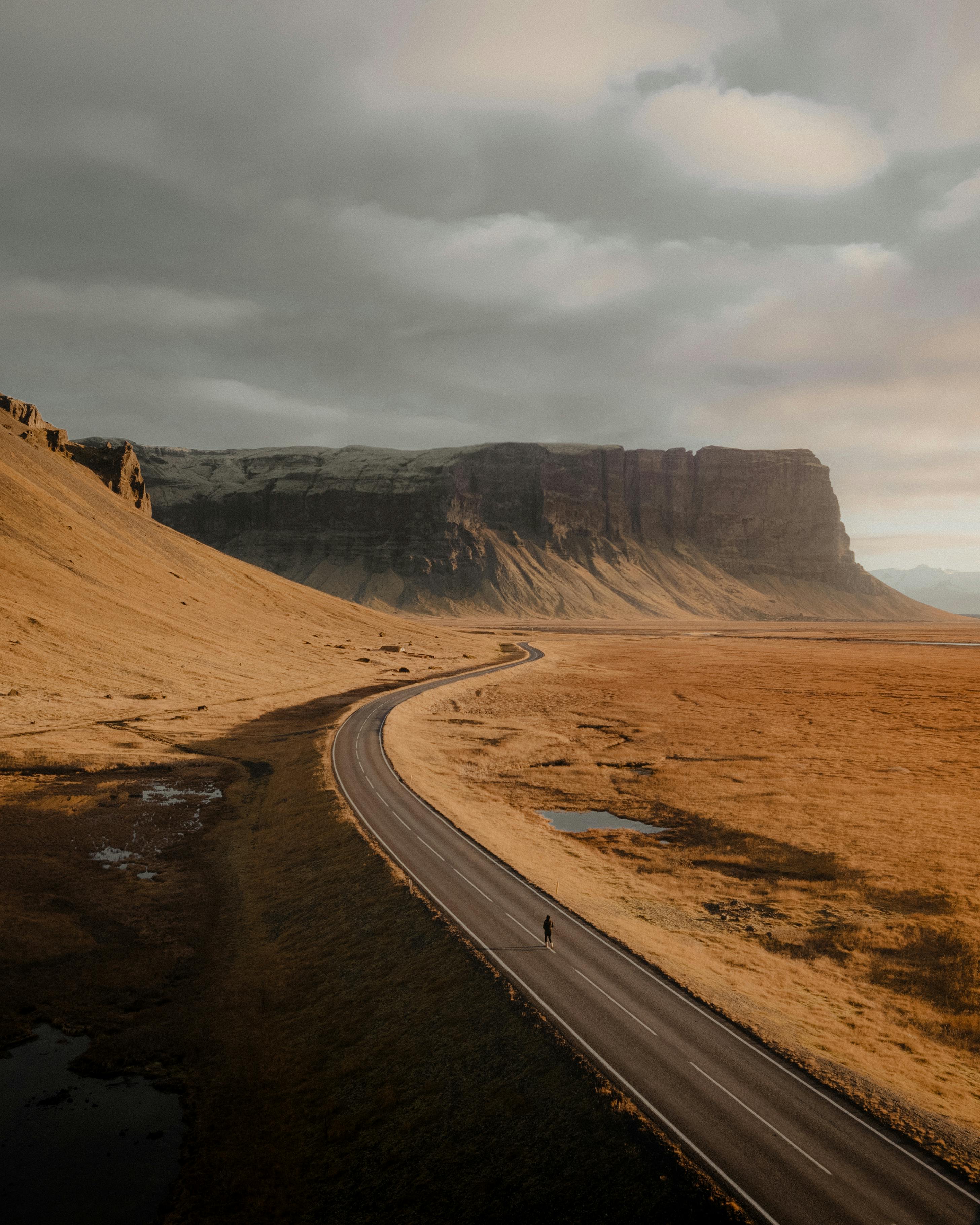 A winding road through the vast, dramatic landscape of Kálfafell, Iceland at sunset.
