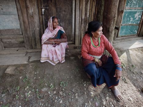 Two elderly women seated on a rustic wooden doorstep in a village, conveying a serene rural lifestyle.