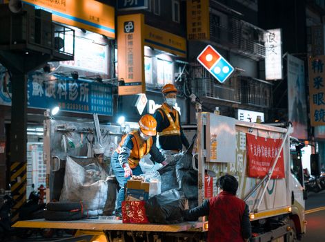 Garbage collectors in safety gear working at night in a vibrant city environment.