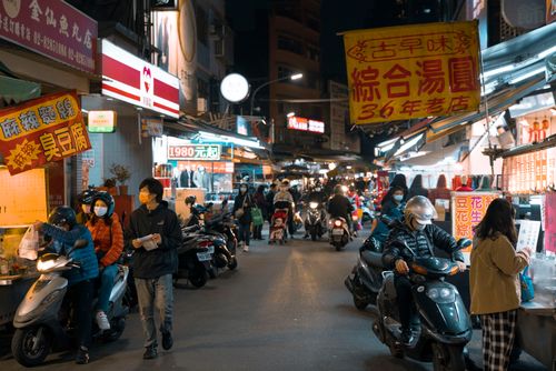 Free A bustling street market at night with people and motorbikes under vibrant signage, capturing urban life. Stock Photo