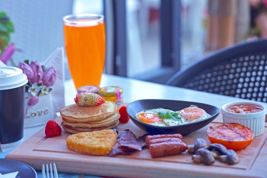 A vibrant breakfast setup featuring pancakes, sunny side up eggs, and fresh juice on a wooden board.