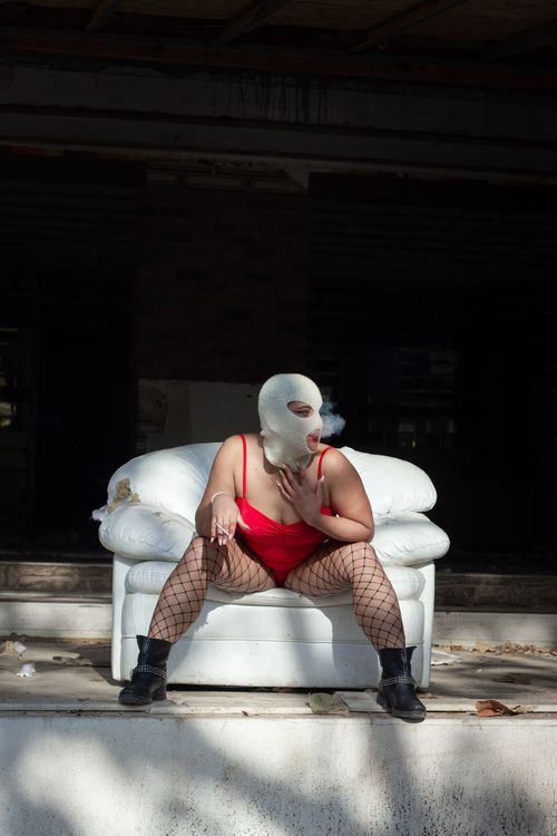 Free A fashion model in a balaclava poses on an armchair while smoking outdoors. Stock Photo