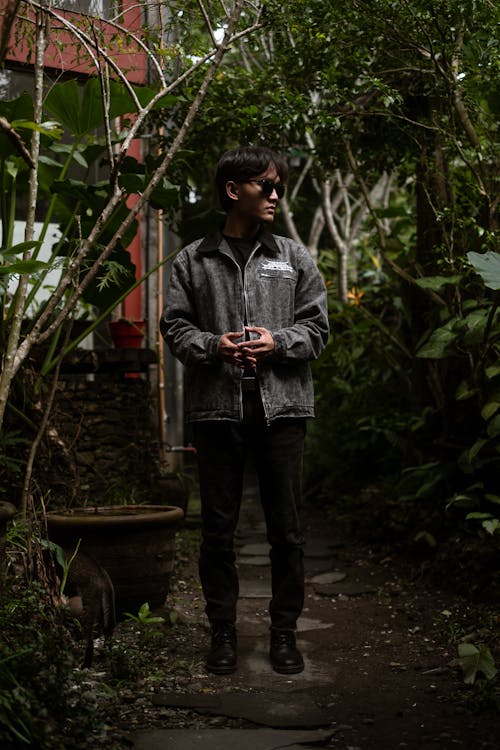 A Man in Denim Jacket Standing Near Green Plants while Looking Afar